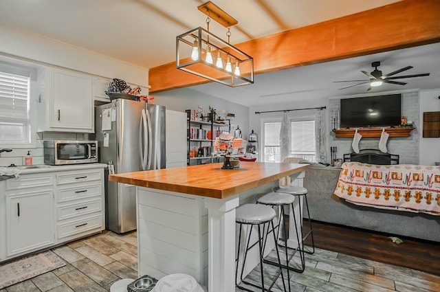 kitchen featuring appliances with stainless steel finishes, white cabinetry, a breakfast bar area, wooden counters, and a center island