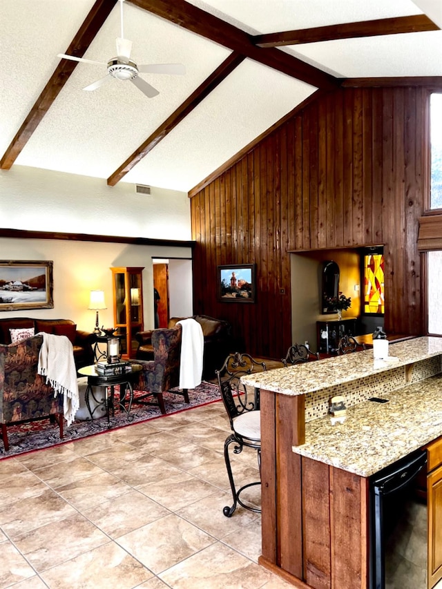 kitchen with vaulted ceiling with beams, wood walls, a textured ceiling, dishwasher, and light stone countertops