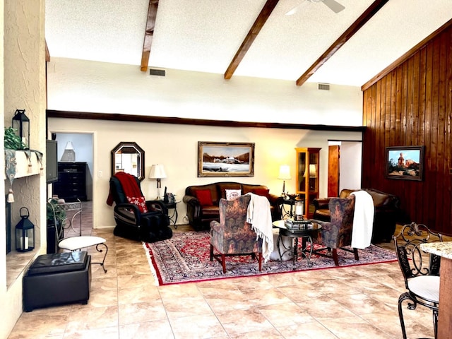 living room with ceiling fan, wooden walls, vaulted ceiling with beams, and a textured ceiling