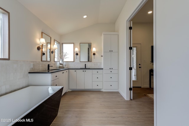 3617 127th St, Lubbock, TX 79423 - bathroom with double vanity, vaulted ceiling, a freestanding tub, wood finished floors, and recessed lighting