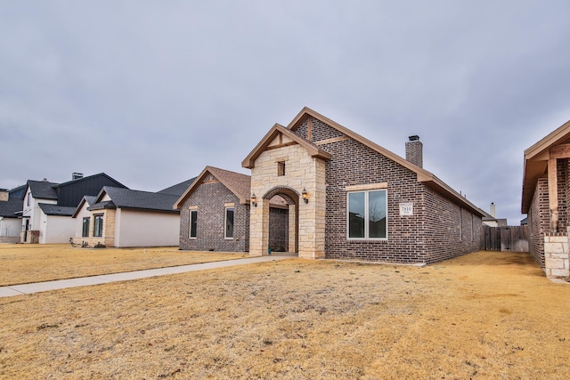 view of front of home featuring stone siding, brick siding, a chimney, and fence