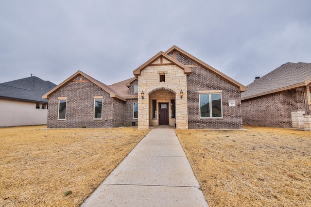 french provincial home featuring stone siding, brick siding, and a front lawn