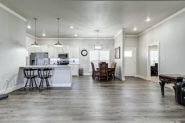 kitchen featuring appliances with stainless steel finishes, a breakfast bar, pendant lighting, white cabinets, and hardwood / wood-style flooring