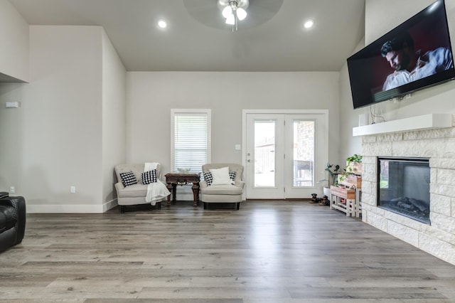 sitting room with hardwood / wood-style flooring, ceiling fan, and a stone fireplace