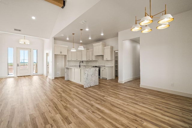 kitchen featuring stainless steel range with electric cooktop, white cabinetry, tasteful backsplash, hanging light fixtures, and an island with sink