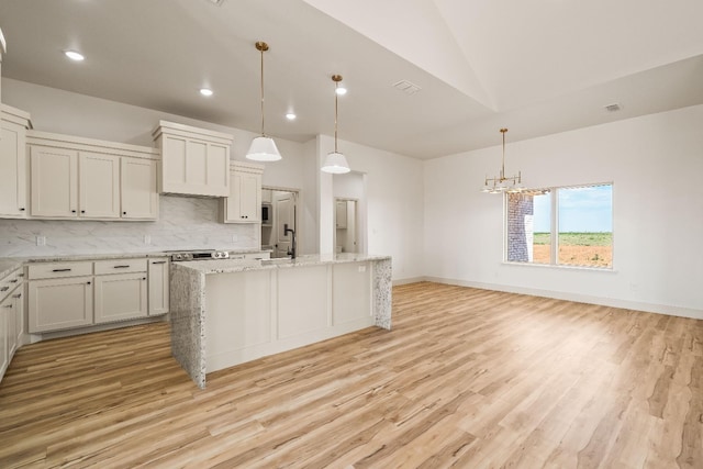 kitchen with tasteful backsplash, light stone counters, pendant lighting, and a center island with sink