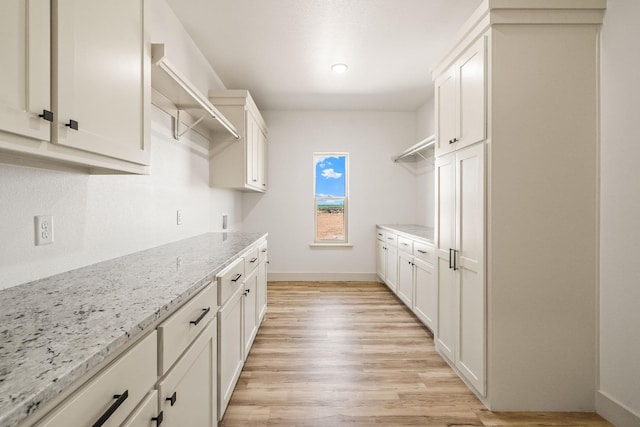 kitchen with white cabinetry, light stone countertops, and light wood-type flooring