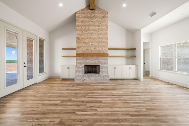 unfurnished living room with beam ceiling, high vaulted ceiling, light hardwood / wood-style floors, a brick fireplace, and french doors