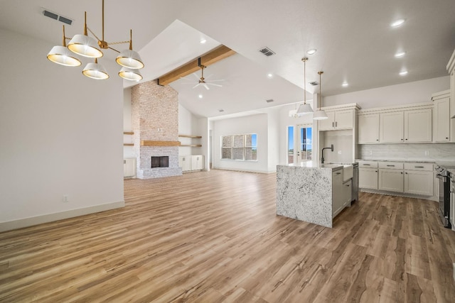 kitchen featuring light hardwood / wood-style flooring, hanging light fixtures, tasteful backsplash, a center island with sink, and a brick fireplace