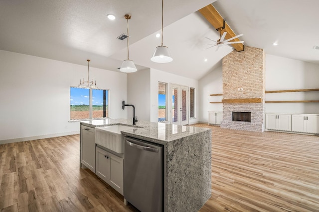 kitchen with hanging light fixtures, stainless steel dishwasher, a large fireplace, light stone countertops, and a kitchen island with sink