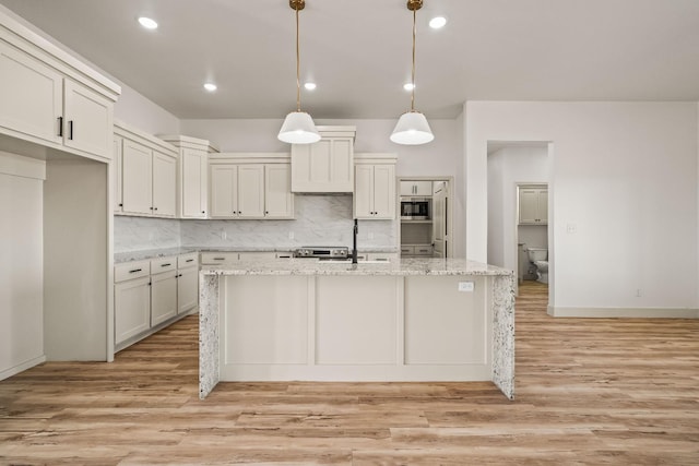 kitchen featuring built in microwave, a kitchen island with sink, pendant lighting, and light stone counters