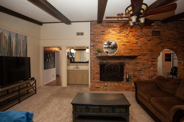 carpeted living room featuring ceiling fan, beam ceiling, sink, and a brick fireplace