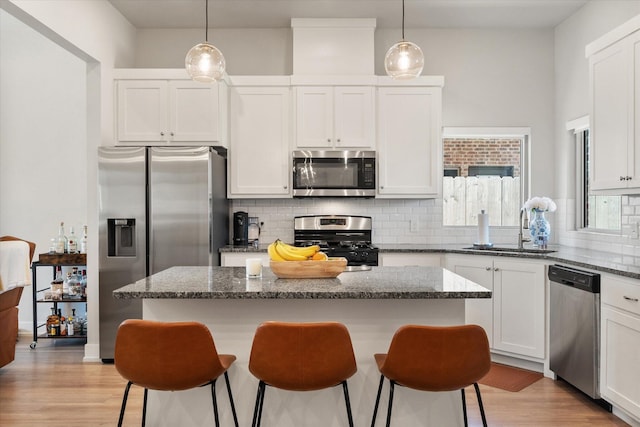 kitchen featuring tasteful backsplash, a breakfast bar, appliances with stainless steel finishes, light wood finished floors, and a sink