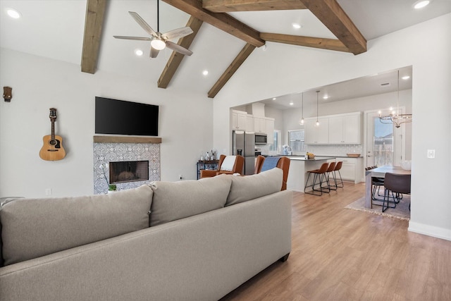living area featuring beam ceiling, a tile fireplace, light wood-type flooring, recessed lighting, and ceiling fan with notable chandelier