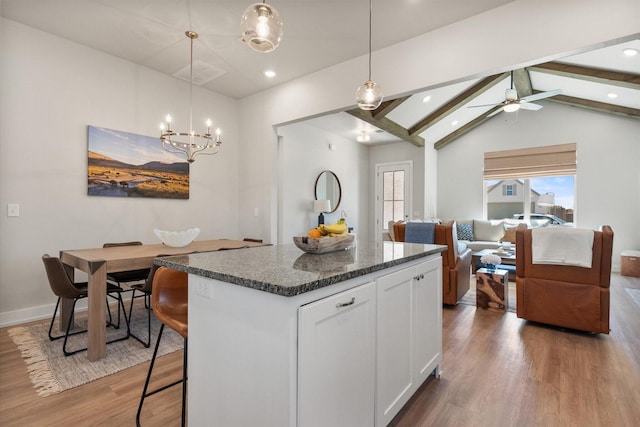 kitchen with dark stone countertops, wood finished floors, vaulted ceiling with beams, a kitchen island, and white cabinets