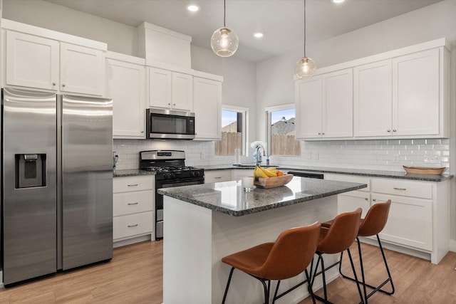 kitchen with appliances with stainless steel finishes, white cabinetry, a kitchen bar, and dark stone countertops