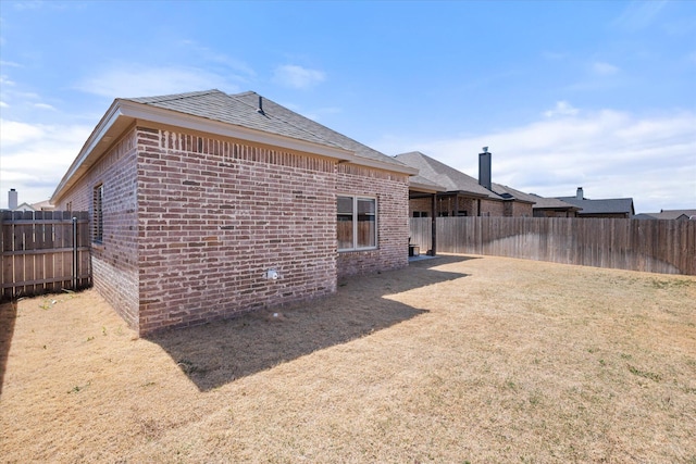 back of house featuring a lawn, a shingled roof, brick siding, and a fenced backyard