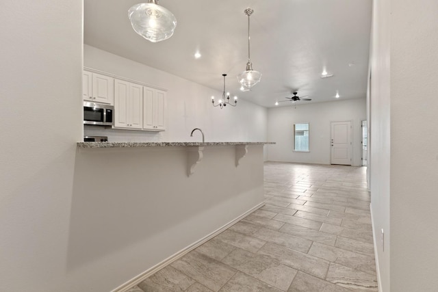 kitchen featuring white cabinetry, a kitchen bar, kitchen peninsula, and hanging light fixtures