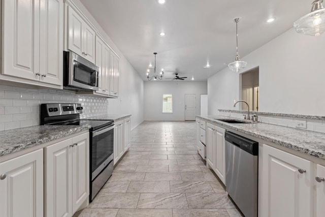 kitchen with appliances with stainless steel finishes, decorative light fixtures, white cabinetry, sink, and light stone counters