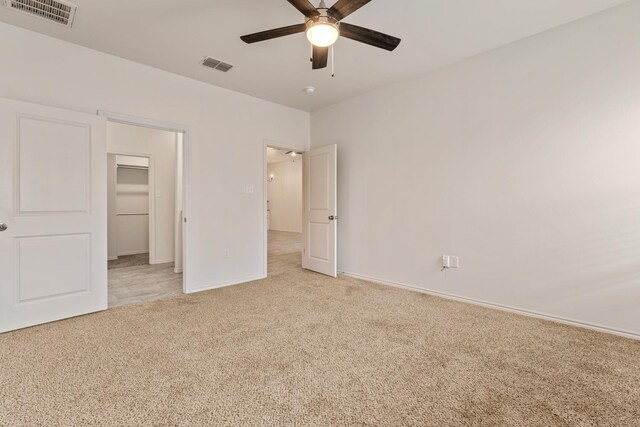 unfurnished bedroom with a walk in closet, light colored carpet, ceiling fan, and a closet