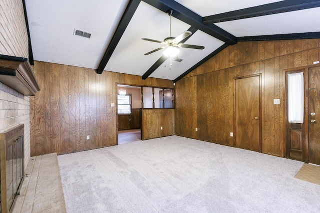 unfurnished living room featuring ceiling fan, wooden walls, a fireplace, lofted ceiling with beams, and light colored carpet