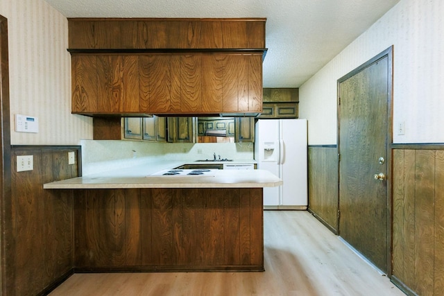 kitchen featuring white appliances, kitchen peninsula, a textured ceiling, and wood walls