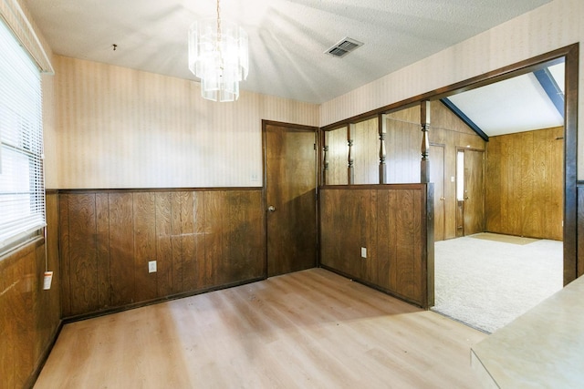 spare room with plenty of natural light, a textured ceiling, a notable chandelier, and wooden walls