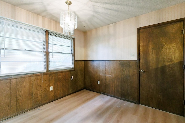 empty room with wooden walls, a chandelier, a textured ceiling, and light wood-type flooring