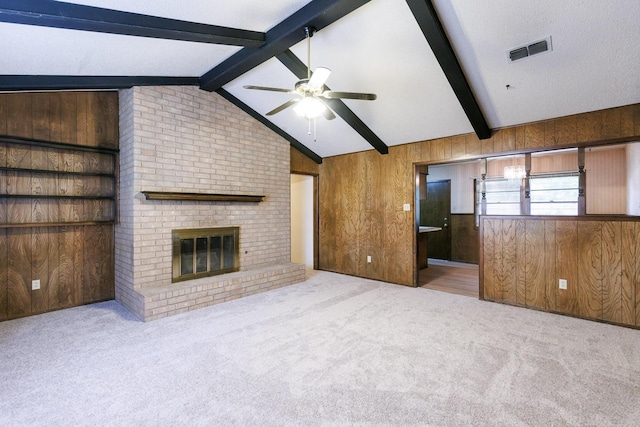 unfurnished living room with wooden walls, vaulted ceiling with beams, ceiling fan, a brick fireplace, and light carpet