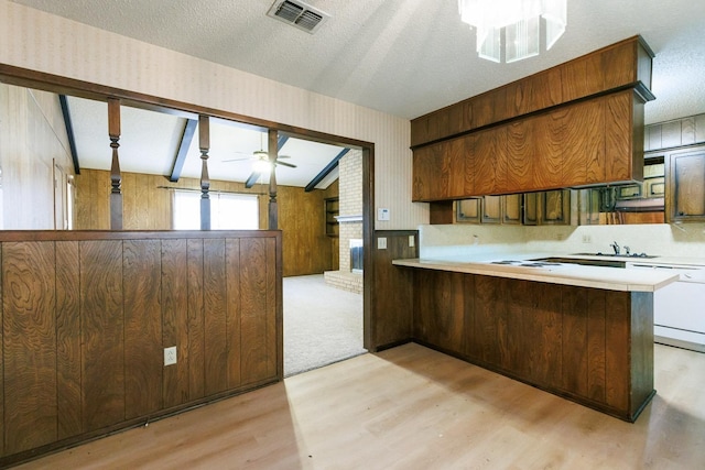 kitchen featuring wooden walls, kitchen peninsula, a textured ceiling, and light hardwood / wood-style flooring