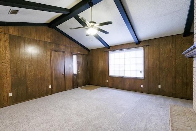 empty room featuring wooden walls, vaulted ceiling with beams, light carpet, and a textured ceiling