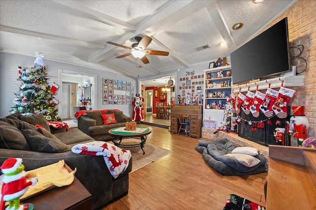 living room featuring lofted ceiling with beams, ceiling fan with notable chandelier, hardwood / wood-style floors, and a textured ceiling