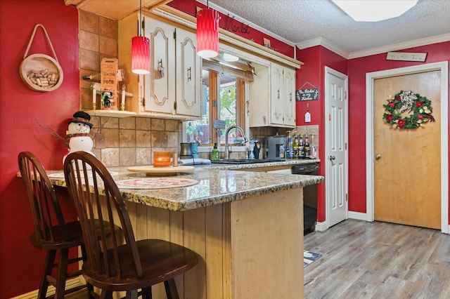 kitchen featuring sink, a kitchen breakfast bar, black dishwasher, light hardwood / wood-style floors, and kitchen peninsula