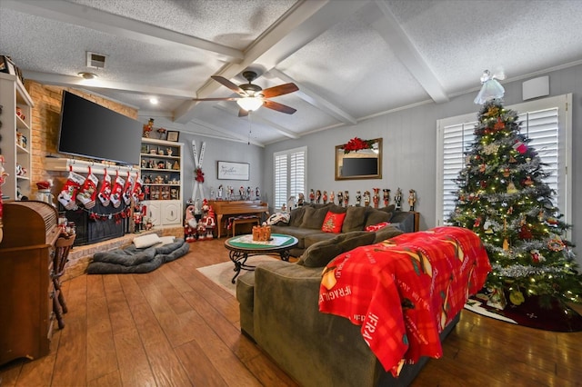 living room with hardwood / wood-style flooring, ceiling fan, vaulted ceiling with beams, a fireplace, and a textured ceiling