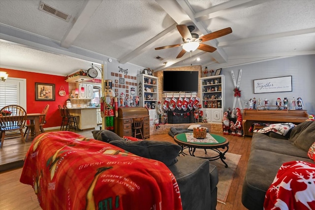 living room with lofted ceiling with beams, a textured ceiling, a large fireplace, hardwood / wood-style flooring, and ceiling fan