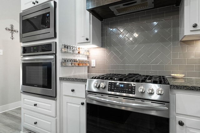 kitchen with white cabinetry, range hood, dark stone countertops, and appliances with stainless steel finishes