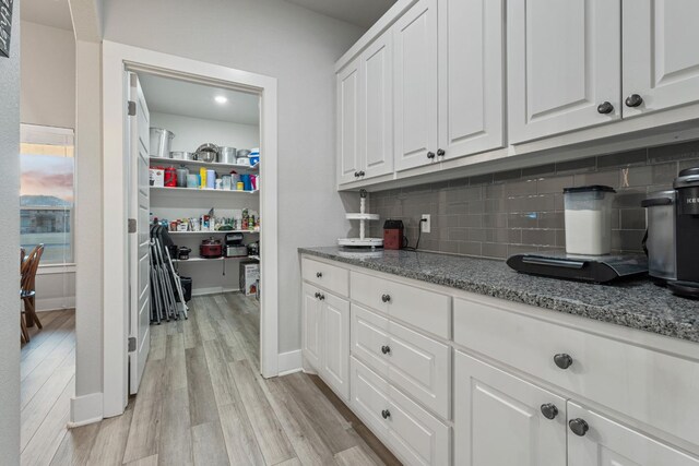 kitchen featuring white cabinetry, light stone countertops, light wood-type flooring, and decorative backsplash