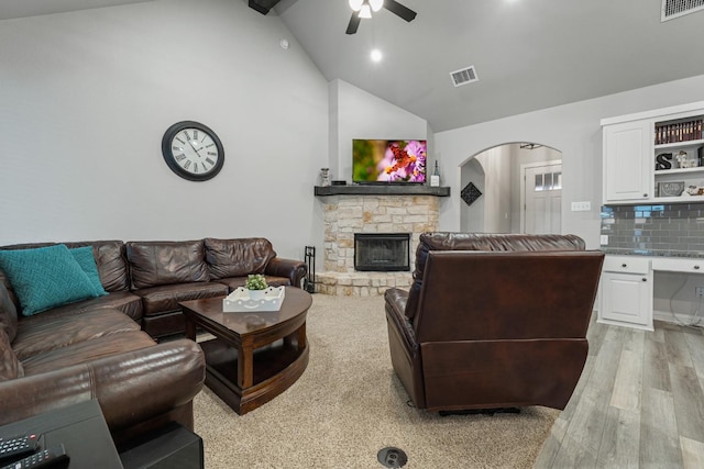 living room with ceiling fan, a stone fireplace, high vaulted ceiling, and light hardwood / wood-style flooring