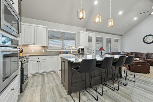 kitchen with a breakfast bar, appliances with stainless steel finishes, white cabinetry, a kitchen island, and dark stone counters