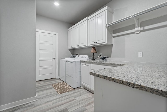 laundry area with washing machine and dryer, cabinets, and light wood-type flooring