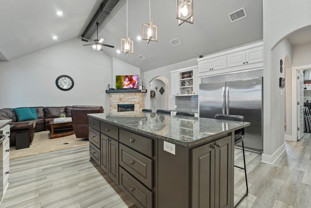 kitchen featuring white cabinetry, dark brown cabinetry, a kitchen bar, a stone fireplace, and built in fridge