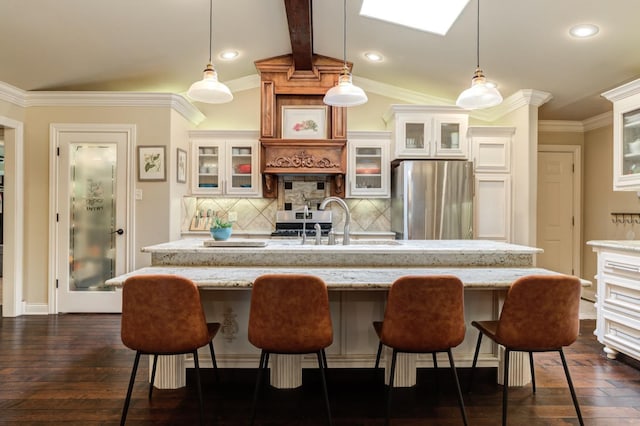 kitchen featuring light stone countertops, a kitchen island with sink, stainless steel fridge, and decorative light fixtures