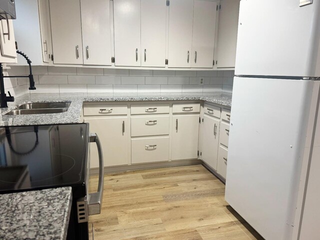 kitchen with black electric range oven, sink, light hardwood / wood-style flooring, white fridge, and decorative backsplash