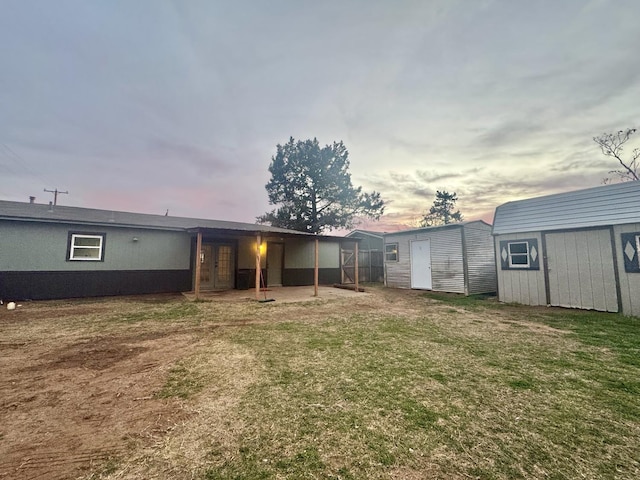 back house at dusk featuring a yard and a storage unit