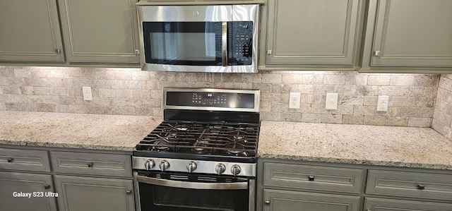 kitchen with light stone countertops, appliances with stainless steel finishes, and backsplash