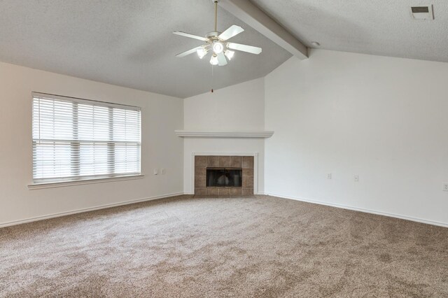 unfurnished living room with a tile fireplace, ceiling fan, vaulted ceiling with beams, carpet floors, and a textured ceiling