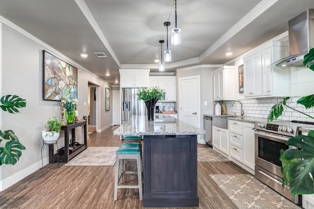 kitchen featuring a center island, wall chimney range hood, a raised ceiling, stainless steel appliances, and white cabinets