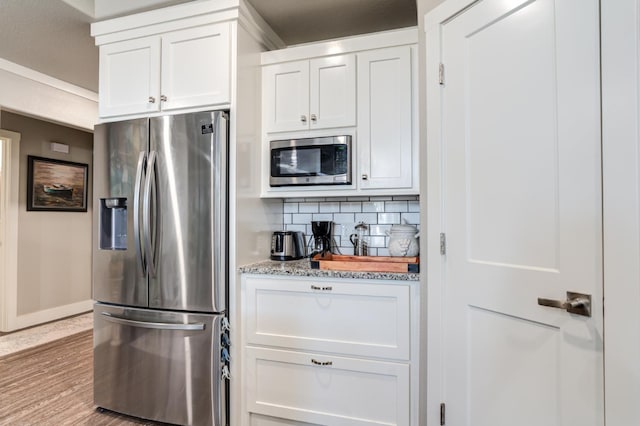 kitchen featuring white cabinetry, decorative backsplash, light hardwood / wood-style floors, light stone counters, and stainless steel appliances