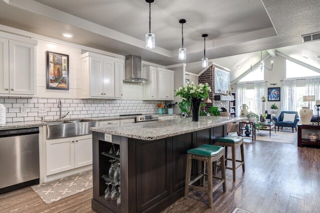 kitchen with white cabinets, a tray ceiling, dishwasher, and wall chimney range hood