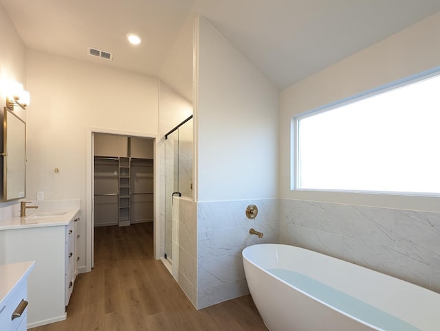 bathroom with lofted ceiling, shower with separate bathtub, tile walls, vanity, and hardwood / wood-style floors